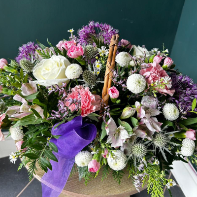 Harmony in Purple - A soothing mix of purple and white flowers, including roses and thistles, arranged in a rustic basket. Ideal for expressing condolences or creating a peaceful ambiance.