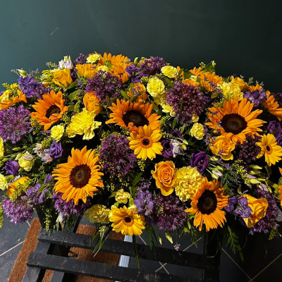 Sunlit Memory - A vibrant funeral arrangement with a warm mix of sunflowers, gerberas, and purple accents, creating a heartfelt tribute that celebrates a life filled with love and joy.