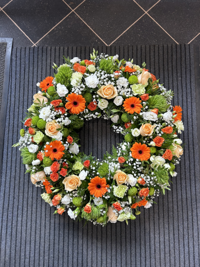 Fresh Glow - A traditional wreath in shades of Orange, peach, greens and whites. Made using a selection of fresh seasonal flowers. 

Product shown is the large option