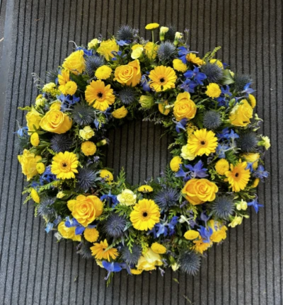 Sunny Sky - Sunny sky is a traditional funeral wreath in shades of yellow and blue.

Made using seasonal flowers this beautiful wreath uses sunny yellows and sky blues to create a bright tribute for a celebration of life. 

Product pictured is the large